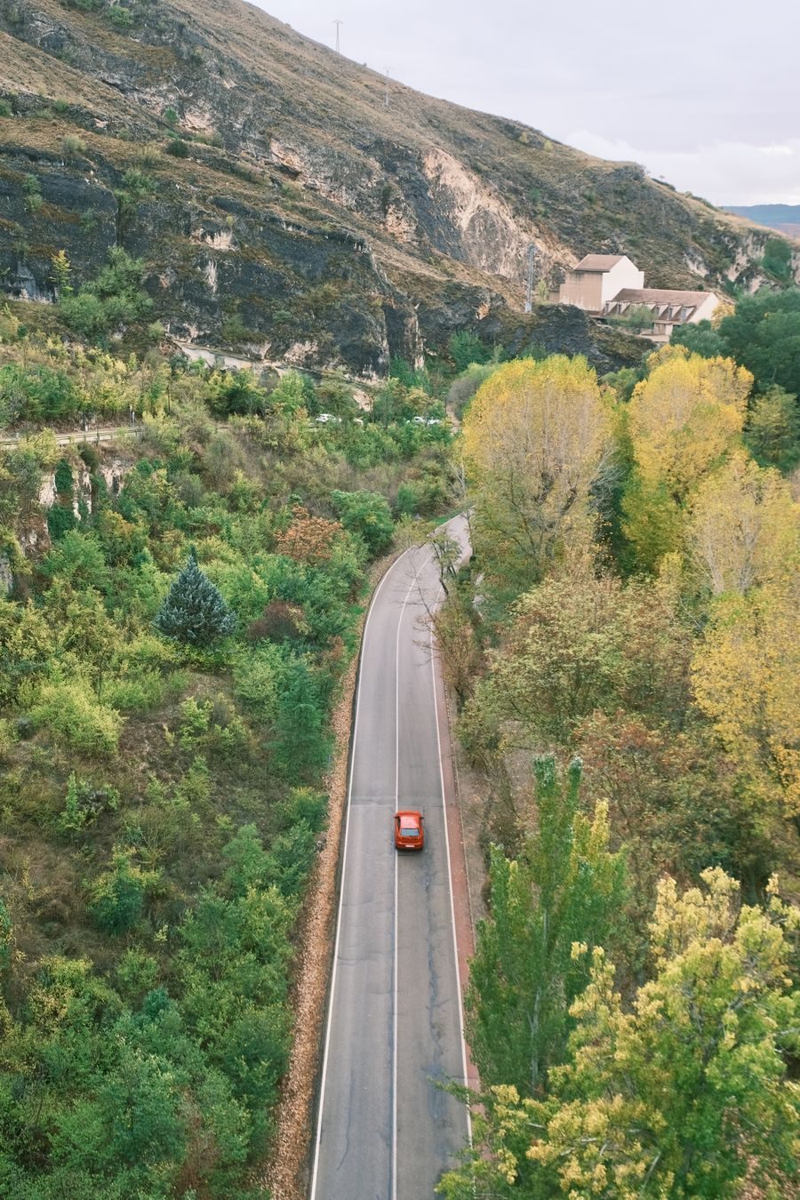 Red car on a winding road through a green valley